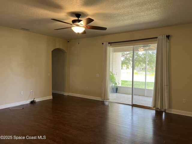 spare room with arched walkways, a textured ceiling, dark wood finished floors, a ceiling fan, and baseboards