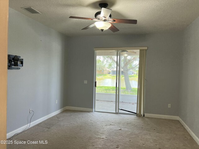 empty room with carpet, a textured ceiling, ceiling fan, baseboards, and a water view