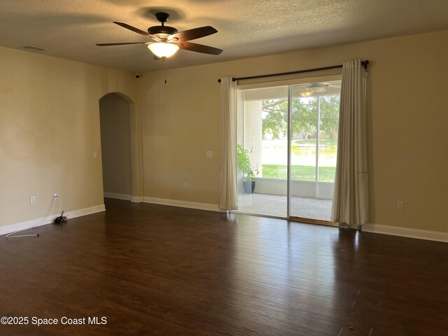 unfurnished room featuring arched walkways, a ceiling fan, dark wood-style floors, baseboards, and a textured ceiling