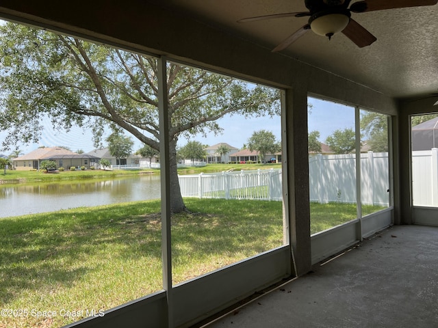 unfurnished sunroom featuring a water view, ceiling fan, and a residential view