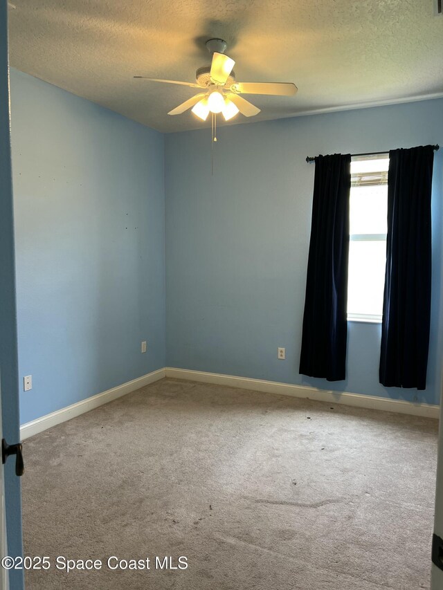 carpeted spare room with a textured ceiling, ceiling fan, and baseboards