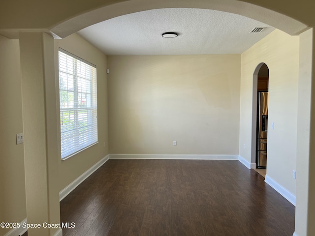 empty room with dark wood finished floors, a textured ceiling, arched walkways, and baseboards