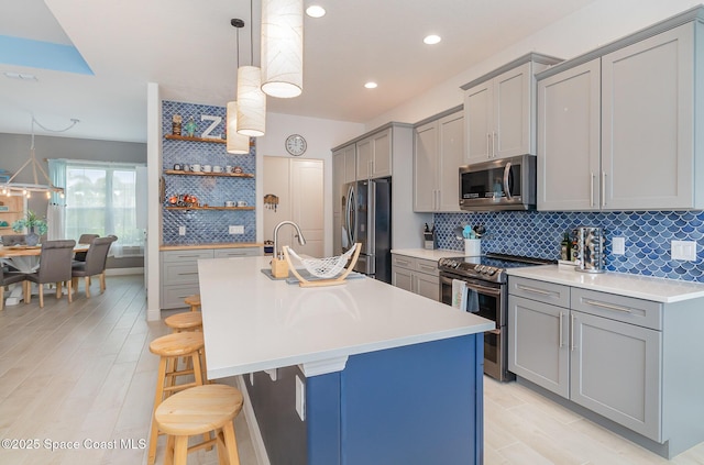 kitchen featuring a breakfast bar, gray cabinets, open shelves, appliances with stainless steel finishes, and light countertops