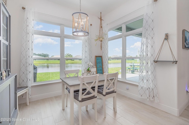 dining space with baseboards, a water view, a chandelier, and light wood finished floors