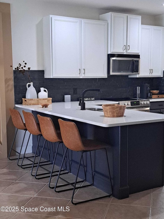 kitchen with tile patterned flooring, stainless steel microwave, backsplash, and a sink