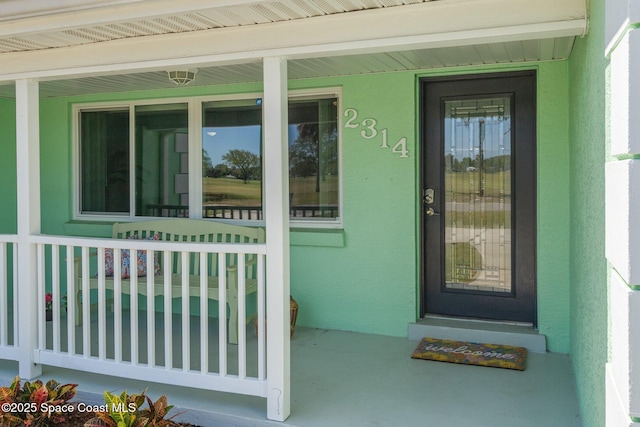 doorway to property featuring covered porch and stucco siding