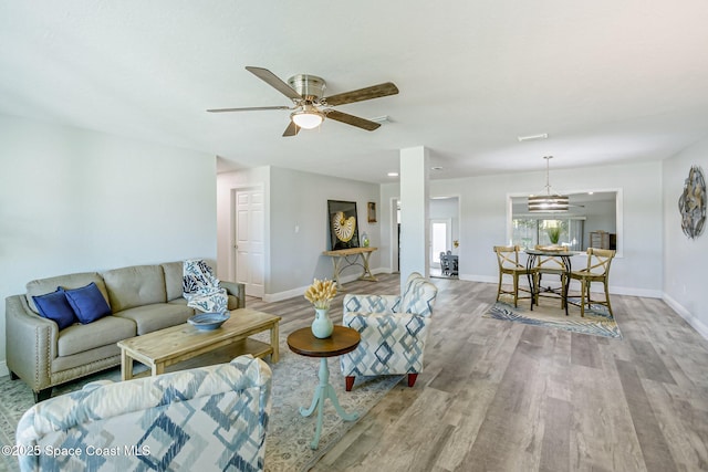 living room featuring a ceiling fan, visible vents, wood finished floors, and baseboards