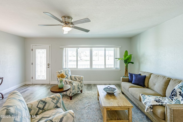 living area featuring baseboards, a textured ceiling, a ceiling fan, and wood finished floors