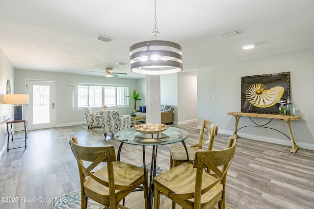 dining area with ceiling fan with notable chandelier, baseboards, visible vents, and light wood finished floors