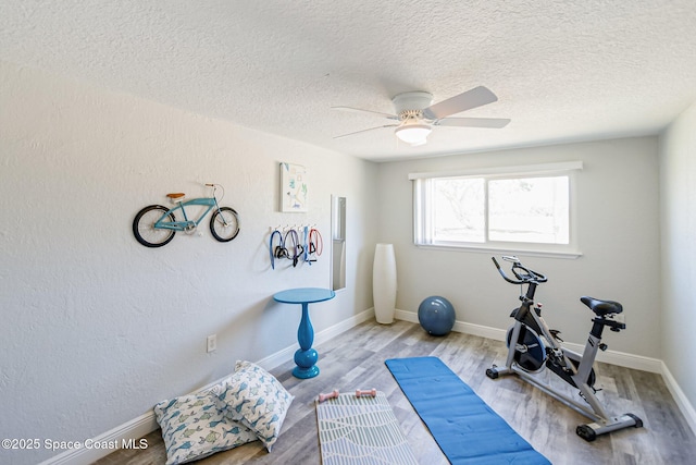 exercise room featuring a textured ceiling, wood finished floors, baseboards, and ceiling fan