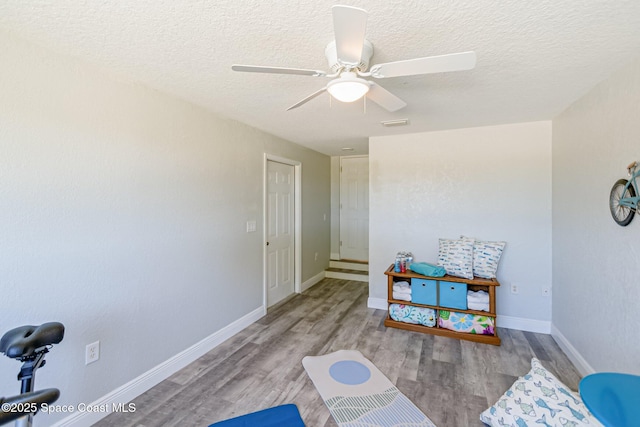 game room with a textured ceiling, ceiling fan, and wood finished floors