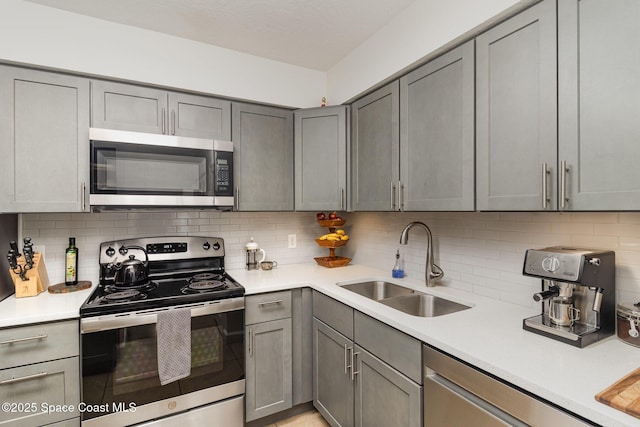 kitchen featuring a sink, stainless steel appliances, backsplash, and gray cabinets