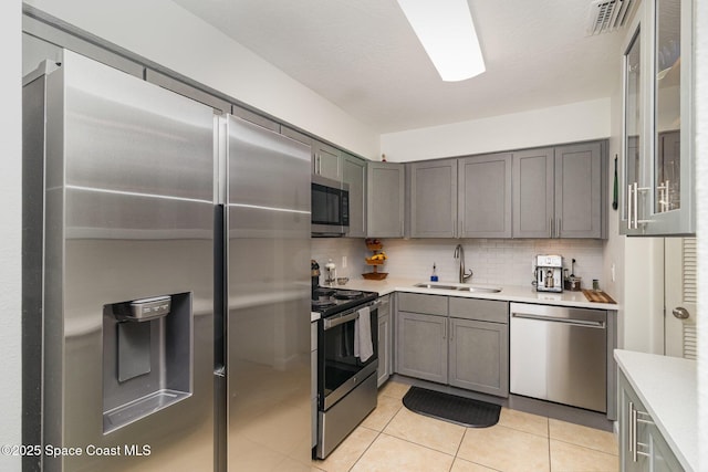 kitchen with a sink, appliances with stainless steel finishes, gray cabinets, and light countertops