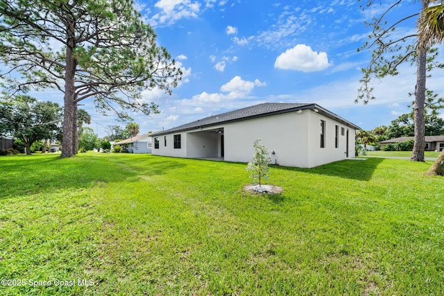 rear view of house featuring a lawn and stucco siding