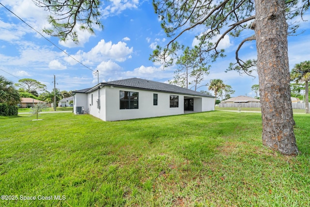 back of property with a yard, central AC, and stucco siding