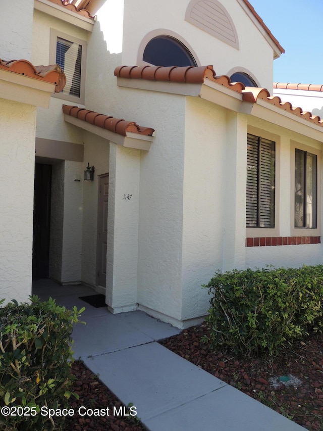 view of exterior entry with stucco siding and a tile roof