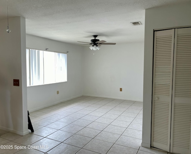 unfurnished room with visible vents, a ceiling fan, a textured ceiling, light tile patterned floors, and baseboards