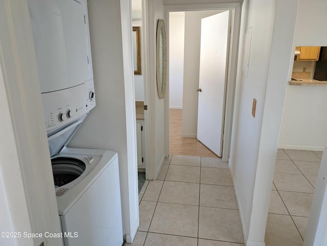 clothes washing area featuring laundry area, light tile patterned flooring, baseboards, and stacked washer and clothes dryer