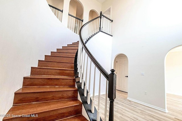 4026 Four Lakes Dr, Melbourne, FL 32940 - staircase featuring baseboards, wood finished floors, arched walkways, and a towering ceiling