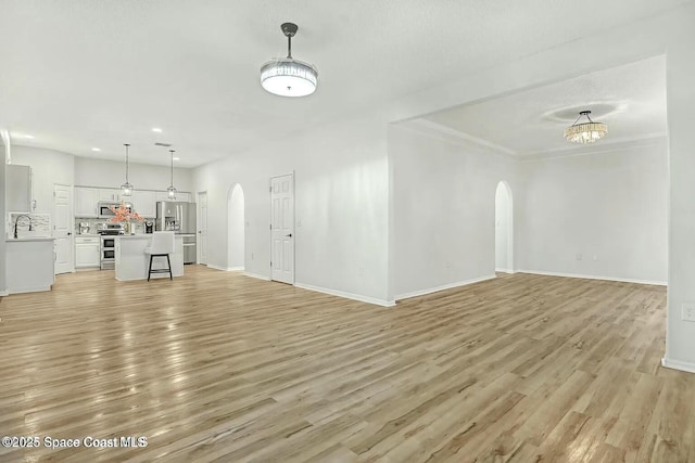 4026 Four Lakes Dr, Melbourne, FL 32940 - unfurnished living room with arched walkways, baseboards, a sink, and light wood finished floors