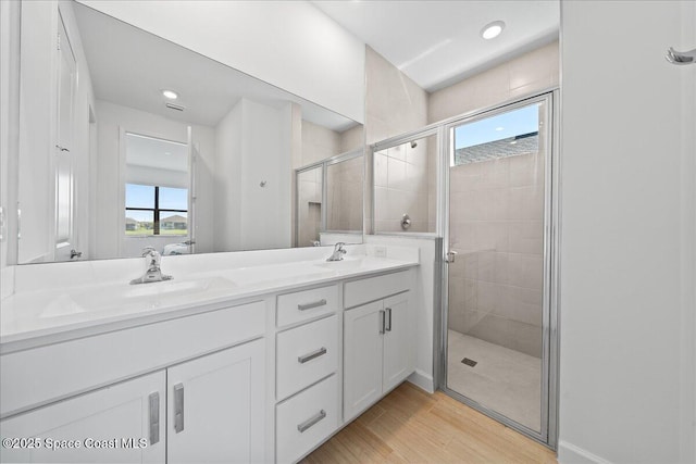 full bath with double vanity, wood finished floors, a stall shower, and a sink