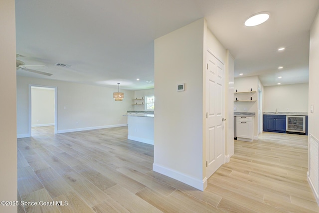 corridor with visible vents, baseboards, beverage cooler, light wood-style flooring, and a sink