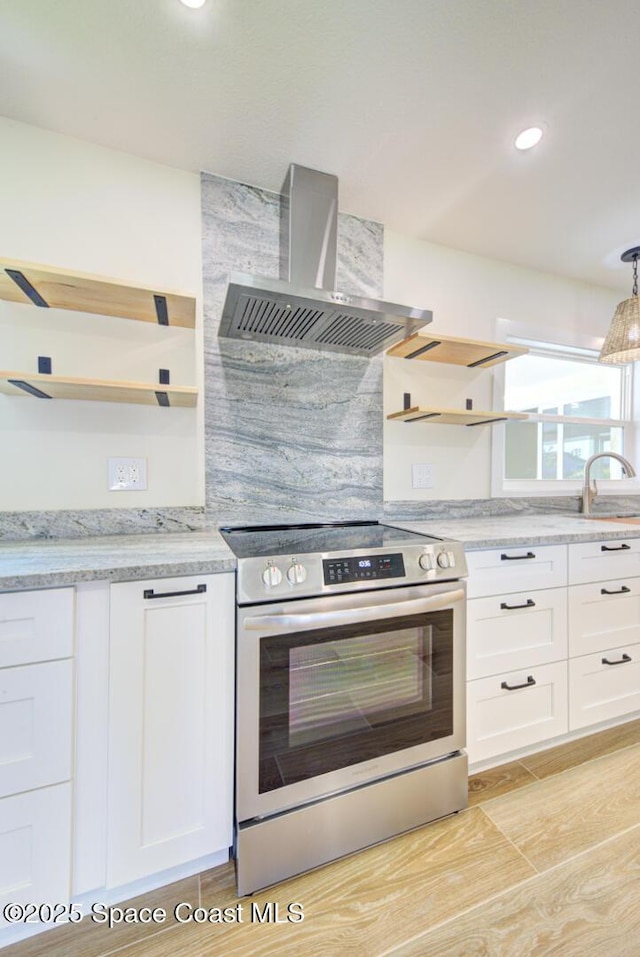 kitchen with stainless steel range with electric cooktop, white cabinetry, wall chimney exhaust hood, and open shelves