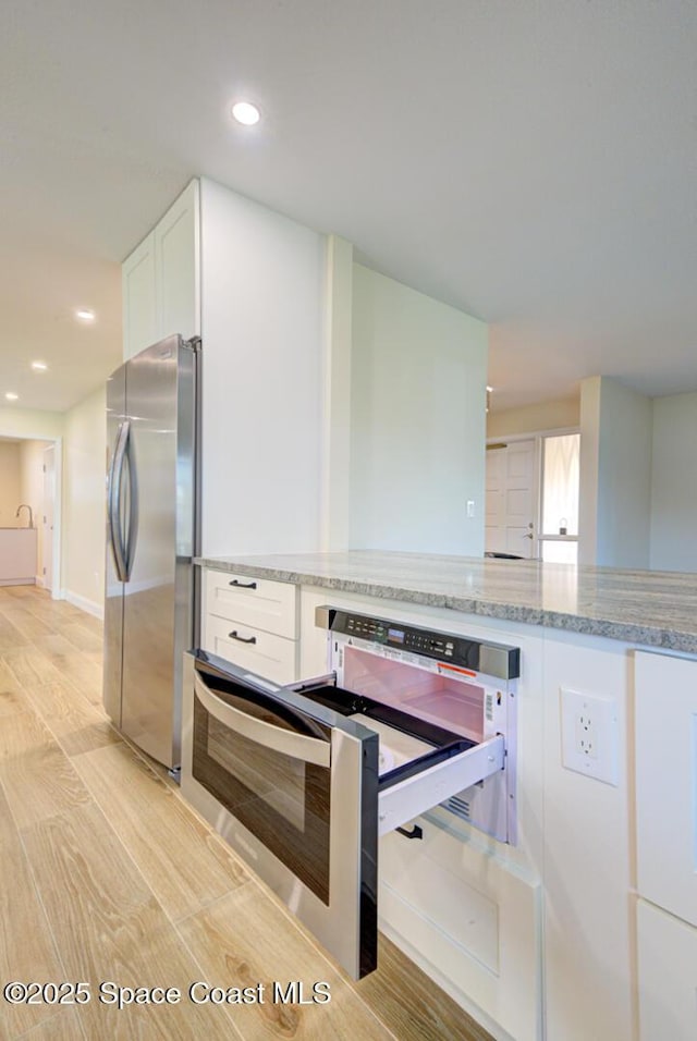 kitchen featuring wall oven, light stone countertops, freestanding refrigerator, light wood-style floors, and white cabinets