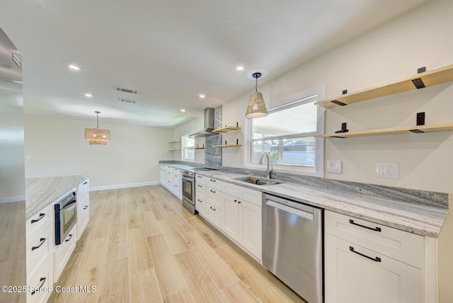 kitchen with open shelves, wall chimney range hood, light wood-style flooring, stainless steel appliances, and a sink