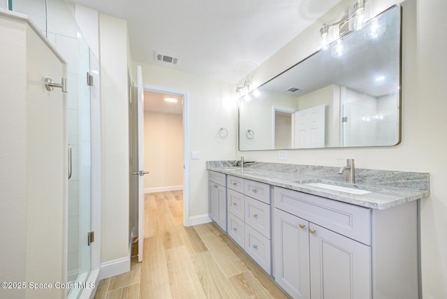 bathroom featuring wood finished floors, visible vents, double vanity, a tile shower, and a sink