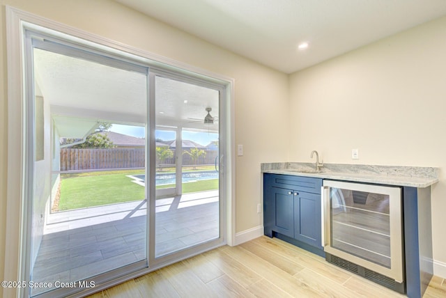 bar with a sink, wine cooler, light wood-style floors, indoor wet bar, and baseboards