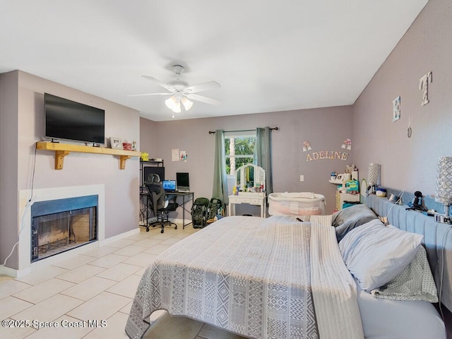 bedroom featuring light tile patterned floors, a fireplace, a ceiling fan, and baseboards