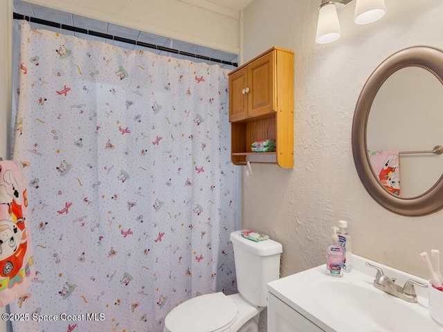 bathroom with vanity, curtained shower, toilet, and a textured wall