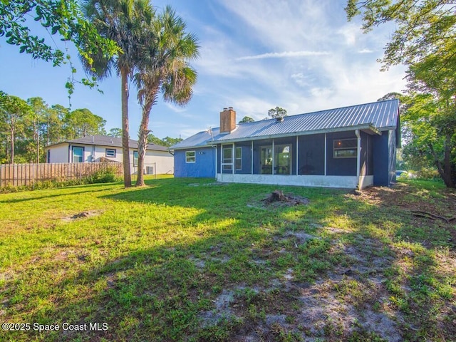 rear view of property featuring fence, metal roof, a chimney, a yard, and a sunroom