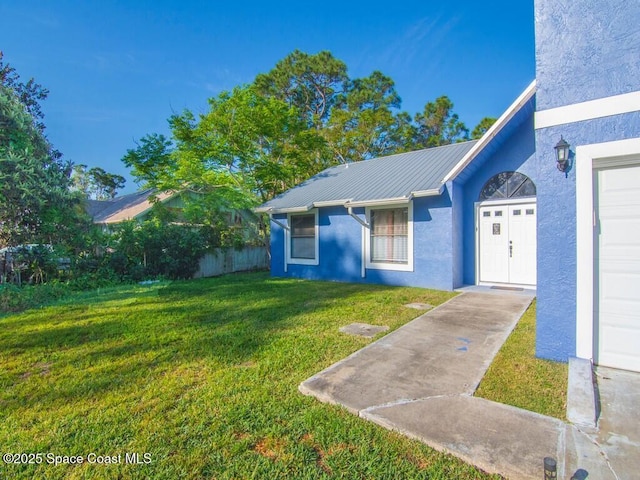 view of front facade featuring a front lawn, fence, stucco siding, metal roof, and a garage