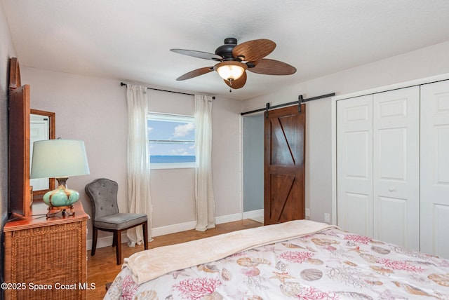 bedroom featuring light wood finished floors, ceiling fan, baseboards, a barn door, and a closet