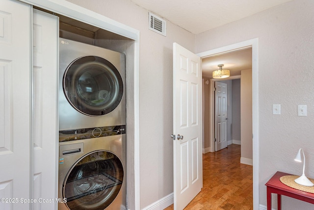 clothes washing area with visible vents, baseboards, stacked washer and dryer, and wood finished floors