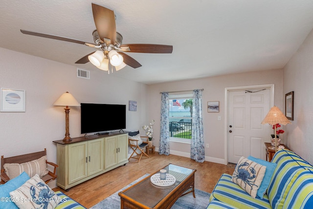 living area with light wood-style flooring, a ceiling fan, visible vents, and baseboards