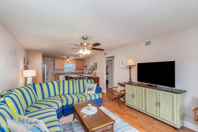 living room featuring visible vents, baseboards, ceiling fan, light wood-style floors, and a textured ceiling