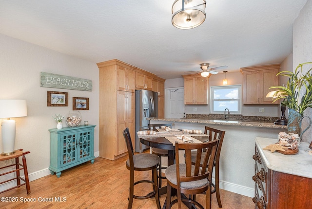 kitchen featuring a ceiling fan, a peninsula, a sink, stainless steel refrigerator with ice dispenser, and light wood-type flooring