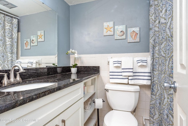 full bath featuring visible vents, toilet, vanity, wainscoting, and tile walls