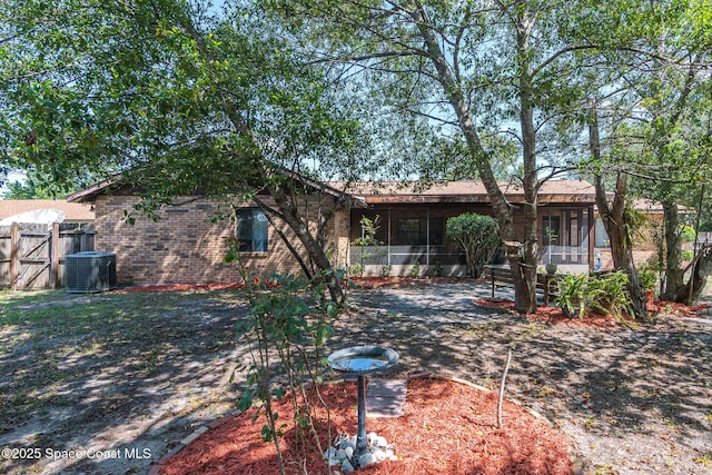 view of front of home featuring a sunroom, brick siding, fence, a gate, and central AC unit