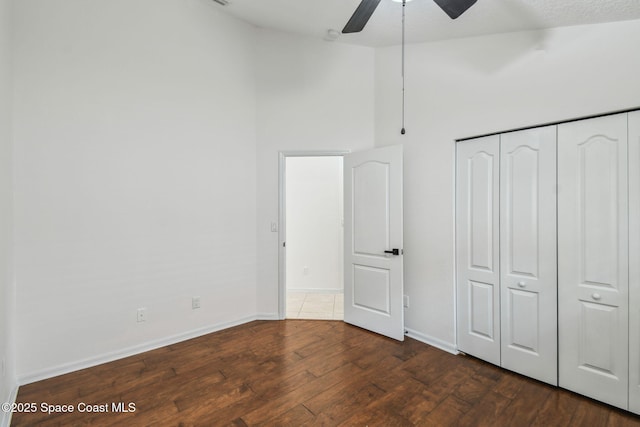 unfurnished bedroom with a towering ceiling, wood finished floors, a ceiling fan, a closet, and baseboards