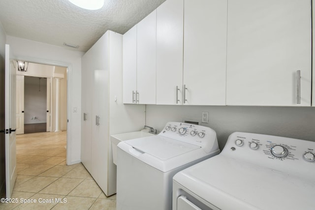 clothes washing area with washer and clothes dryer, a textured ceiling, light tile patterned floors, and cabinet space