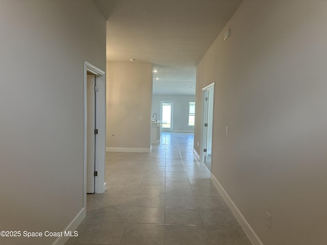 hallway featuring light tile patterned flooring, baseboards, and a textured ceiling