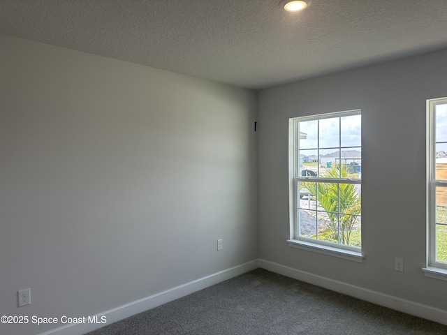 empty room featuring plenty of natural light, dark carpet, a textured ceiling, and baseboards