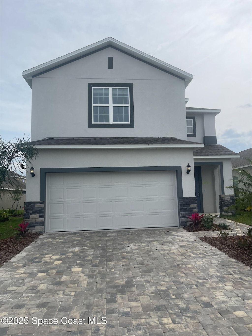 traditional-style home with decorative driveway, stone siding, an attached garage, and stucco siding