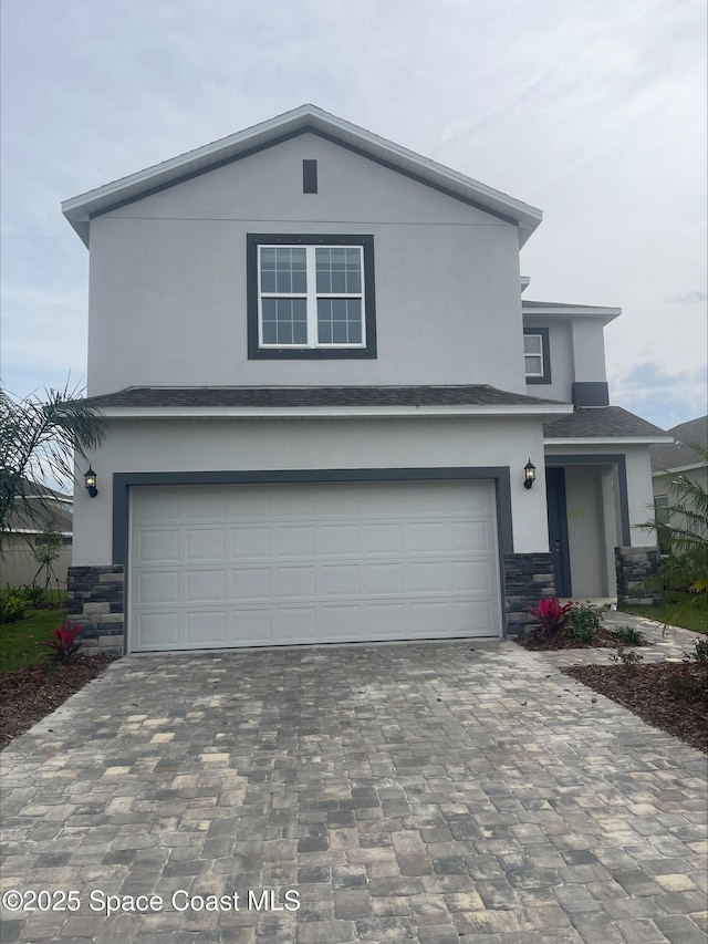 traditional-style home with decorative driveway, stone siding, an attached garage, and stucco siding