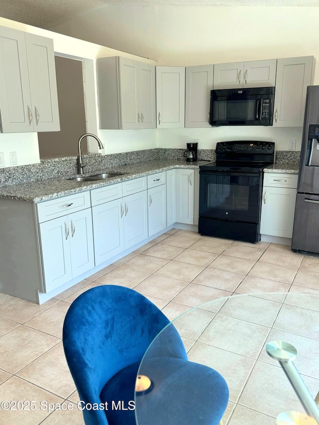 kitchen featuring light tile patterned floors, light stone countertops, black appliances, and a sink