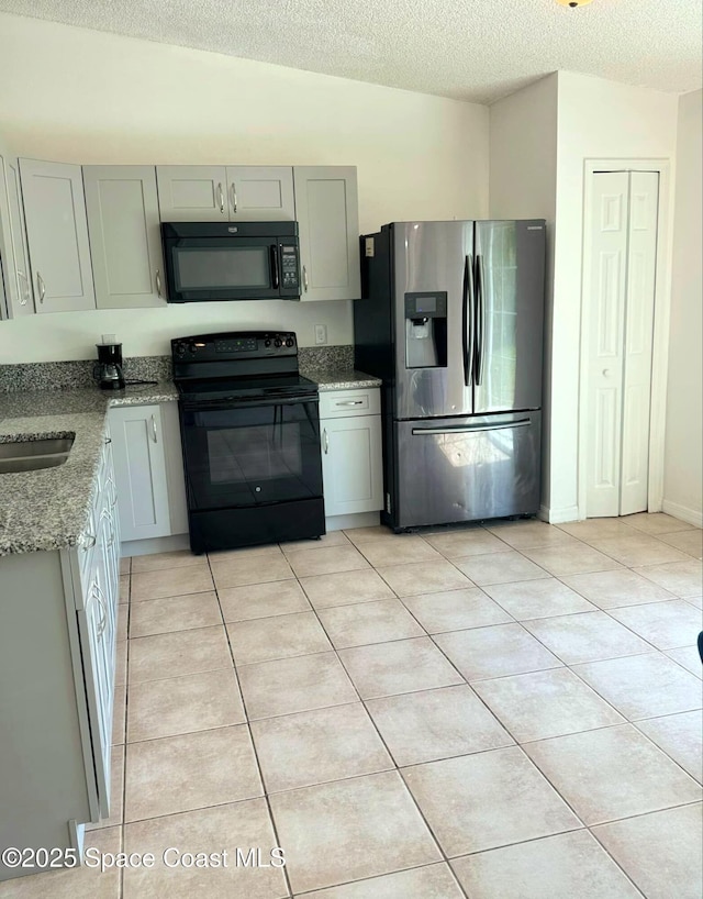 kitchen with light tile patterned floors, light stone countertops, a textured ceiling, and black appliances